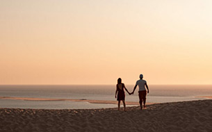 Couple se tenant la main devant un coucher de soleil sur la dune du Pilat